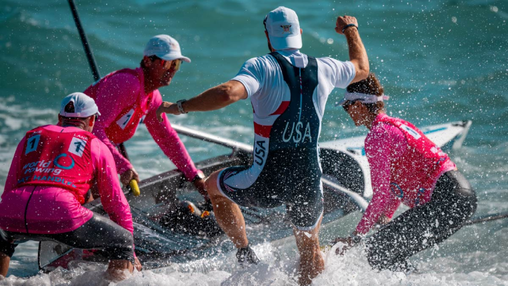 Marc Oria helps hold the boat as Chris Bak runs through the surf at the 2024 World Rowing Beach Sprint Finals.