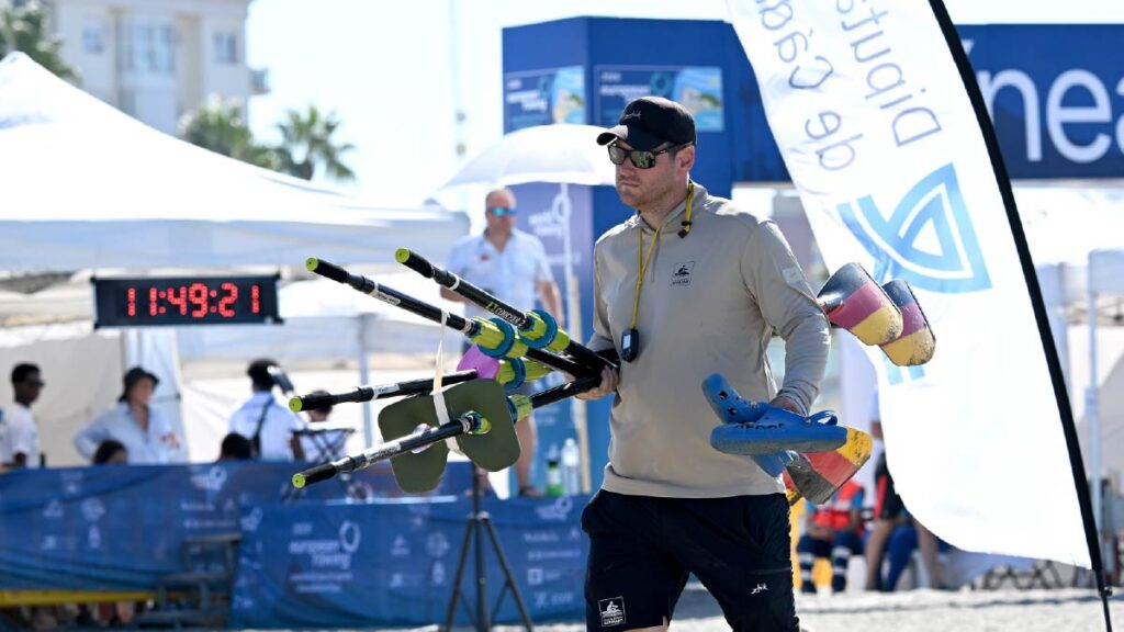 Head coach Adrian Bretting carries his athletes' equipment